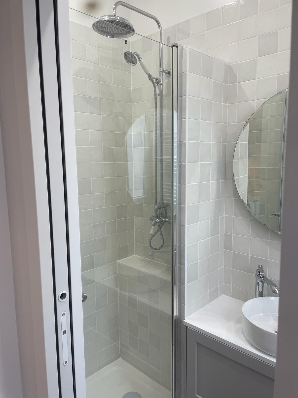 Une salle de bain blanche avec une douche, un lavabo, un miroir et du carrelage blanc et gris