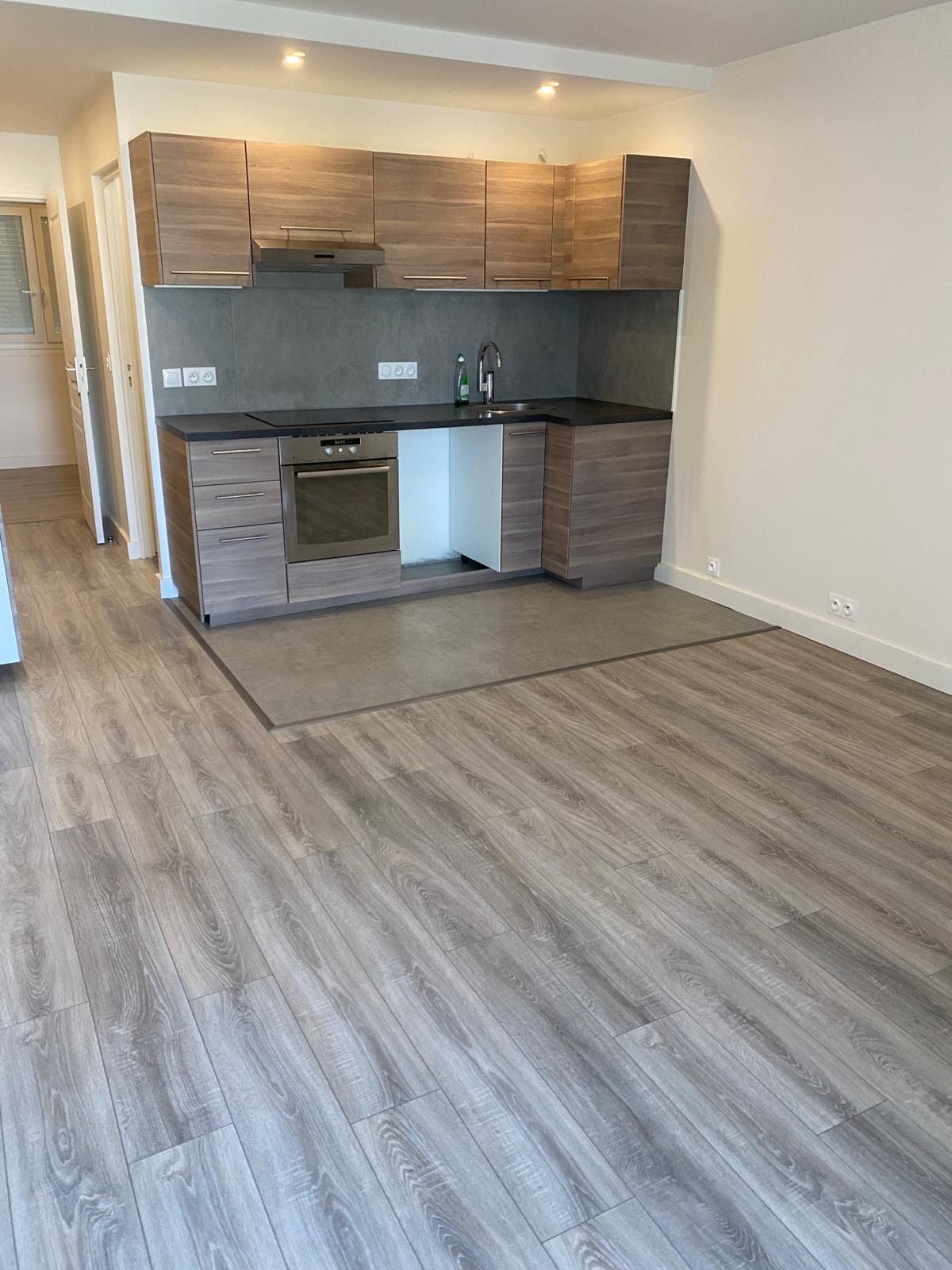 Une pièce avec un parquet posé et une cuisine avec des façades en bois 