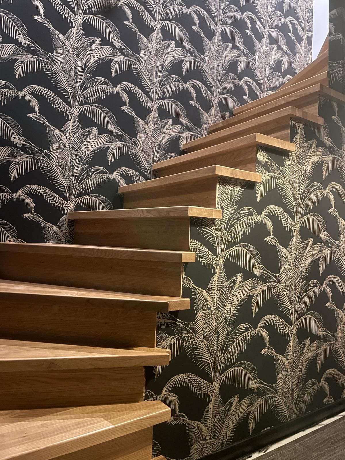 Des escaliers en bois avec une tapisserie représentant des palmiers en noir et blanc